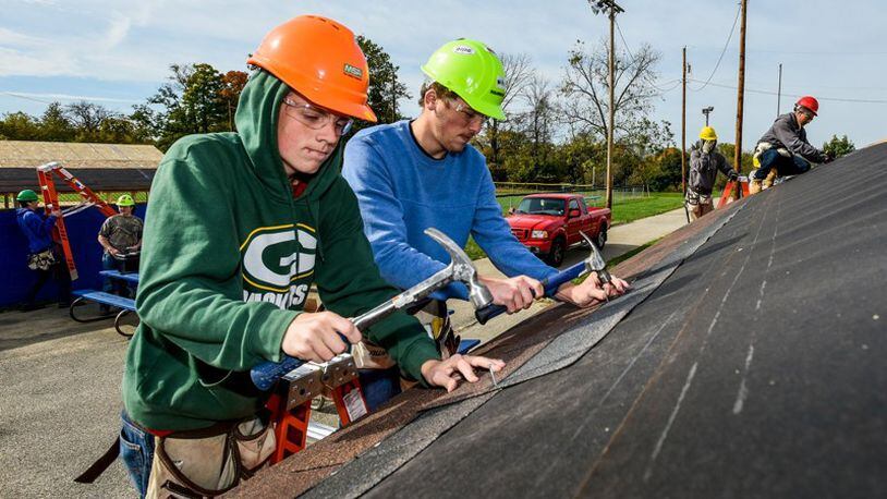 Ryan Kemp, left, and Nicholas Caudill, right, seniors in the Butler Tech construction technologies program, puts shingles on the roof at the baseball dugouts at Crawford Woods Park along Hancock Avenue in Hamilton. NICK GRAHAM/STAFF