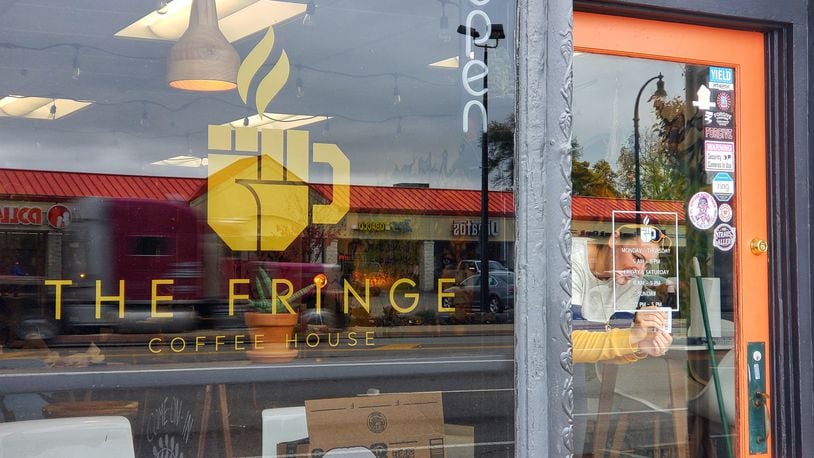 Ashley Ingle installs hours signage to the front door of The Fringe Coffee House, which is scheduled to open Thursday, Oct. 29, 2020 in Hamilton. NICK GRAHAM / STAFF