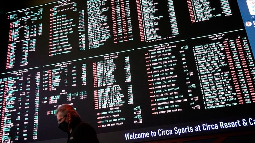 A man walks by as betting odds for NFL football's Super Bowl 55 are displayed on monitors at the Circa resort and casino sports book, Wednesday, Feb. 3, 2021, in Las Vegas. (AP Photo/John Locher)