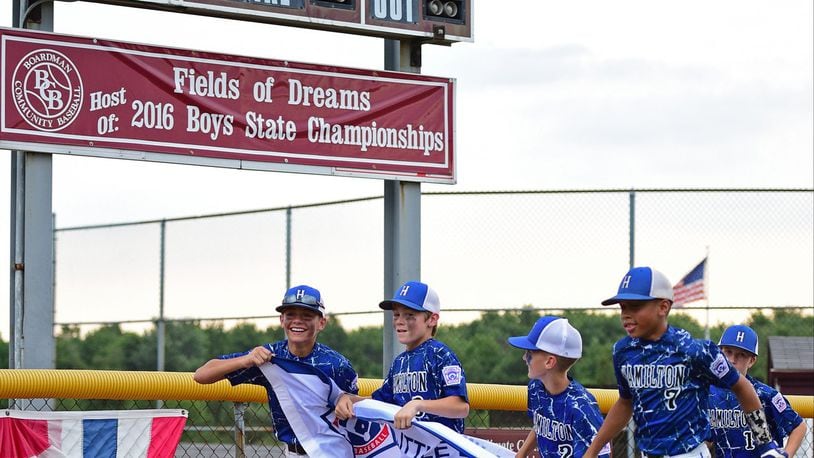 Hamilton West Side’s Landyn Vidourek (4), Maddox Pennington (3), Charlie Vidourek (2) and Braedyn Moore (7) run with their championship banner in front of the scoreboard after Sunday’s 11-0 victory over Canfield in the Ohio Little League championship game at Boardman’s Fields of Dreams. DAVID DERMER/SPECIAL TO THE JOURNAL-NEWS