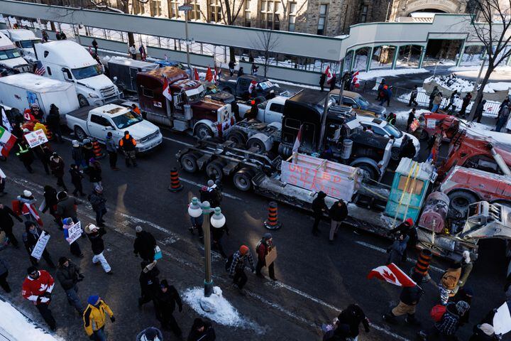 Protesters walk alongside trucks parked in downtown Ottawa, part of a convoy organized in response to a recent regulation that requires truckers returning from the U.S. to show proof of vaccination, in Ottawa, Canada, Jan. 29, 2022. Justin Trudeau, the country’s prime minister, lashed out on Monday, Jan. 31, at the demonstrators, chastising them for desecrating war memorials, wielding Nazi symbols and stealing food from the homeless. (Nasuna Stuart-Ulin/The New York Times)