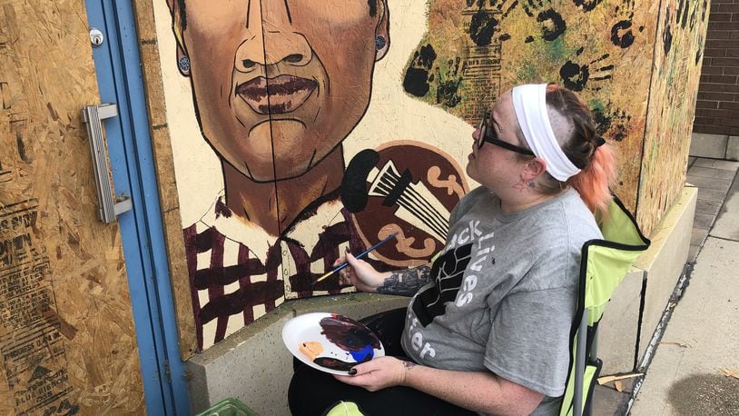Artist Ashli Szymanski finishes a portrait of Elijah McClain on plywood outside a Middletown downtown business. The mural includes four portraits and Szymanski plans to add more. RICK McCRABB/STAFF