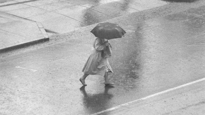 A woman walks on a rain-filled street in downtown Hamilton. Journal-News File Photo