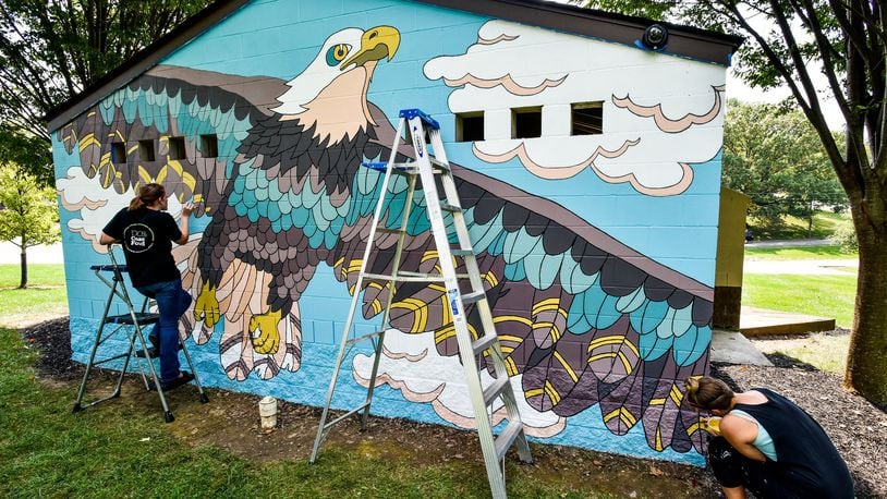 Melissa Smith (left) and Jenn Acus-Smith paint a mural on the restroom building at Veterans Park on New London Road in Hamilton. Acus-Smith designed murals for different locations in Hamilton parks. NICK GRAHAM/STAFF