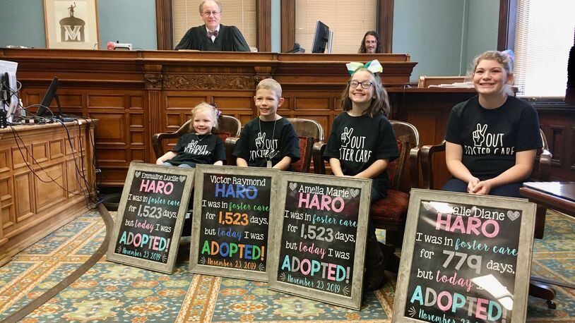 Four formally foster children of the Haro family proudly display their homemade signs - as presiding Butler County Common Pleas Probate Judge Randy Rogers looks on from bench - noting their days in in the foster system. Rogers granted the legal adoption Saturday of (L-R) 4-year-old Emmaline Haro; 8-year-old Victor; 9-year-old Amelia and 13-year-old Rosalie Hora to their new mother and father, Dani and Matt Haro. (Photo By Michael D. Clark/Journal-News)