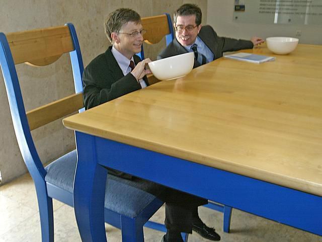 Bill Gates looks at an empty oversized bowl on a giant kitchen table AP