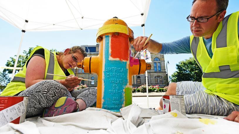 Last year, Morgan Gattermeyer, left, and Stephen Smith with Inside Out Studio painted a fire hydrant along High Street. The city of Hamilton has partnered with the YMCA and InsideOut Studio to paint about 275 fire hydrants throughout the city in either safety yellow or a creative design. NICK GRAHAM/STAFF