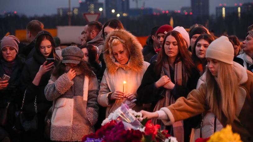 People lay flowers and light candles standing next to the Crocus City Hall, on the western edge of Moscow, Russia, Saturday, March 23, 2024. Russia's top state investigative agency says the death toll in the Moscow concert hall attack has risen to over 133. The attack Friday on Crocus City Hall, a sprawling mall and concert venue on Moscow's western edge, also left many wounded and left the building a smoldering ruin. (AP Photo/Alexander Zemlianichenko)