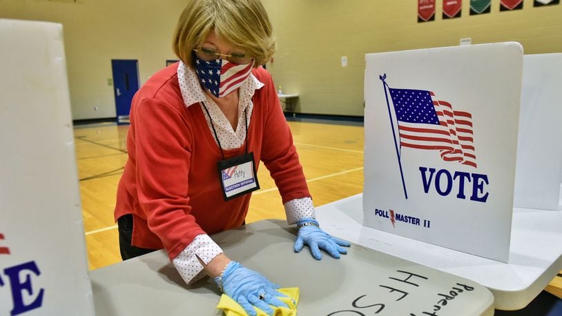 Poll worker Patty Mays cleans a table between voters on election day at the polling location at Wilson Middle School Tuesday, Nov. 3, 2020 in Hamilton. NICK GRAHAM / STAFF
