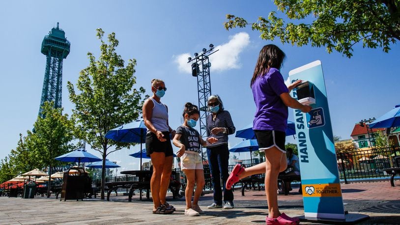 A family demonstrates the use of a hand sanitizer station during media day at Kings Island Wednesday, July 1, 2020 in Mason. Kings Island opens to pass holders July 2 with numerous protocols in place to decrease the chance of spread of COVID-19. Guest must pre-register for admission to the park and are required to wear masks, get their temperature taken and stand in accordance with social distancing guidelines. There are also hundreds of hand sanitizers stations around the park and staff cleaning rides, games, restaurants and touch surfaces regularly. NICK GRAHAM / STAFF