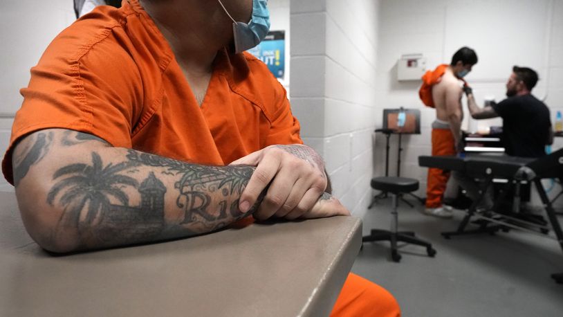 Gilberto watches and waits his turn, as Jamie prepares to have a bullet scar hidden with a tattoo at the DuPage County Jail, Thursday, Feb. 3, 2022, in Wheaton, Ill. To get the jail's backing in their job hunts, participants must graduate. And to graduate, they must have their gang tattoos removed or covered with non-gang tattoos. It's proof they're serious about forsaking their old lives and aren't merely pining for leniency from their jailers or judges, said DuPage County Sheriff James Mendrick. (AP Photo/Charles Rex Arbogast)