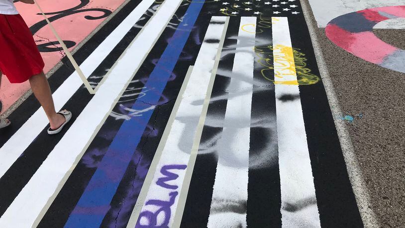 A Lakota West High School student's pro-police art work - depicting the "thin blue line" on an American flag painting - in a parking space was vandalized. Both school and police leaders criticized the crime. Pictured, students, school staffers restoring the artwork, which had included anti-police profanity. (Provided Photo\Journal-News)