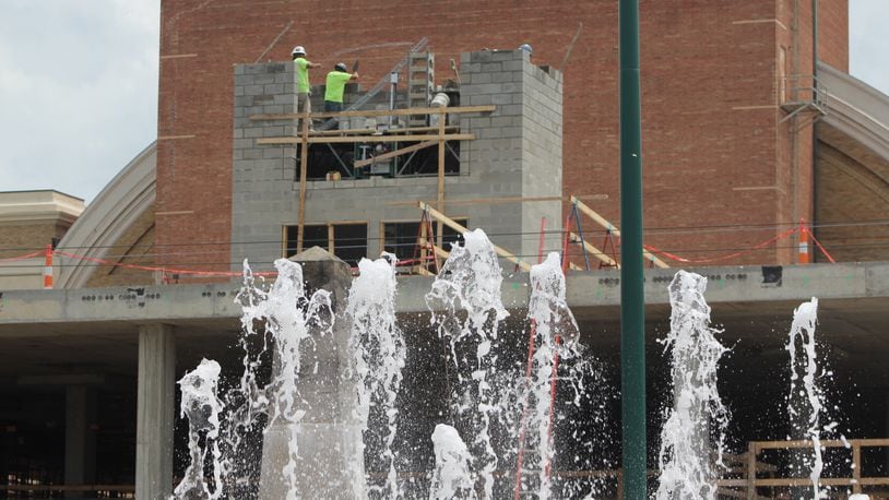 Construction crews work on a new apartment building across from RiverScape MetroPark in downtown Dayton as the fountains operate. CORNELIUS FROLIK / STAFF