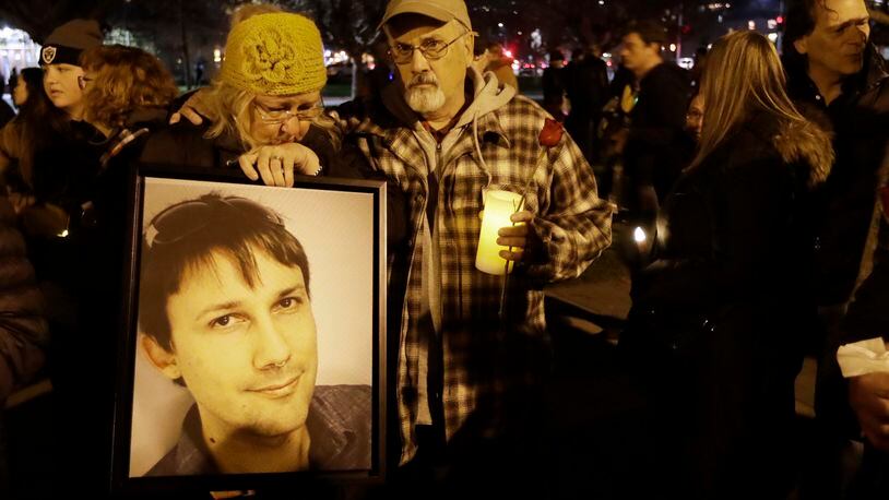 Judy Hough, left, and her husband Brian, center, hold a picture of their son Travis, who died in a warehouse fire, during a vigil at Lake Merritt on Monday, Dec. 5, 2016, in Oakland, Calif. Family members and friends are being notified as firefighters continue a painstaking search for victims of the Oakland warehouse fire. (AP Photo/Marcio Jose Sanchez)