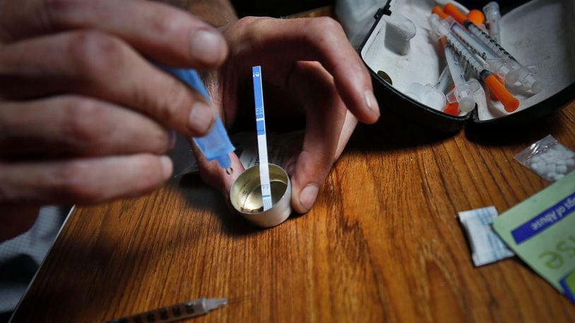 An addict prepares heroin, placing a fentanyl test strip into the mixing container to check for contamination. FILE PHOTO