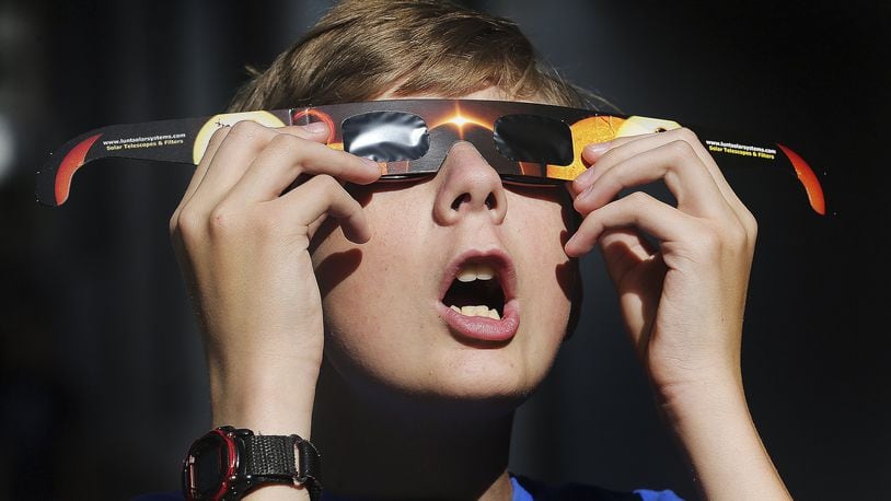 In this Wednesday, Aug. 16,photo, Colton Hammer tries out his new eclipse glasses he just bought from the Clark Planetarium in Salt Lake City in preparation for the eclipse. (Scott G Winterton/The Deseret News via AP)