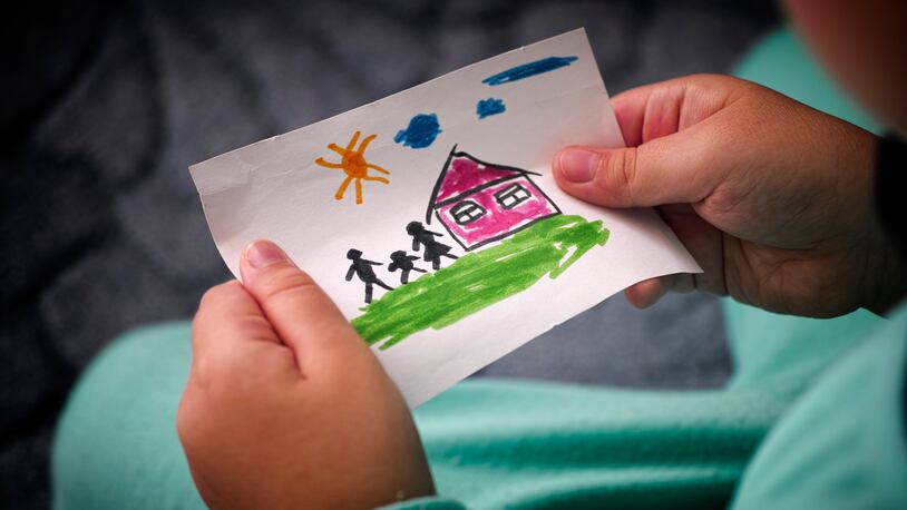 Child holds a drawn house with family.