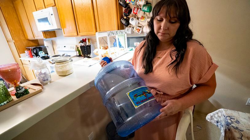 I Richelle Dietz holds an empty five-gallon water bottle at her home in Joint Base Pearl Harbor-Hickam, Monday, April 22, 2024, in Honolulu, Hawaii. The Dietz family relies on bi-weekly water deliveries for basic needs since their water was tainted in 2021. (AP Photo/Mengshin Lin)