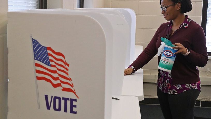 Camille Hall, from the Clark County Board of Elections, wipes down voting booths for early voters Wednesday. The Board of Elections is taking steps to make sure polling places are clean and virus free. BILL LACKEY/STAFF