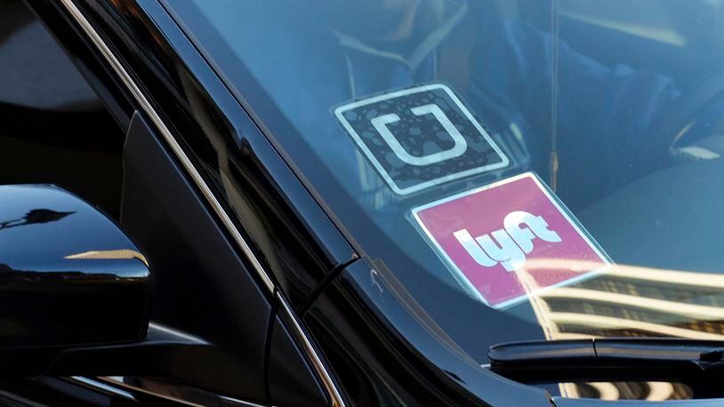 FILE - In this Tuesday, Jan. 12, 2016, file photo, a driver displaying Lyft and Uber stickers on his front windshield drops off a customer in downtown Los Angeles. California regulators on Thursday, Nov. 9, 2017, adopted new safety rules for ride-hailing companies Uber and Lyft that will not require their drivers be fingerprinted as part of background checks, rejecting a push by the taxi industry. (AP Photo/Richard Vogel, File)