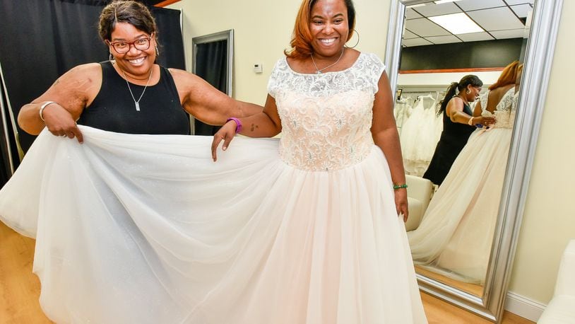 Owner Jonda Prather, left, holds a dress for Jennifer Norman as they finalize looks for a wedding themed photo shoot Wednesday, June 26 at Belle Bridal Boutique on Central Avenue in Middletown. Prather says her shop specializes on plus size bridal gowns. NICK GRAHAM/STAFF
