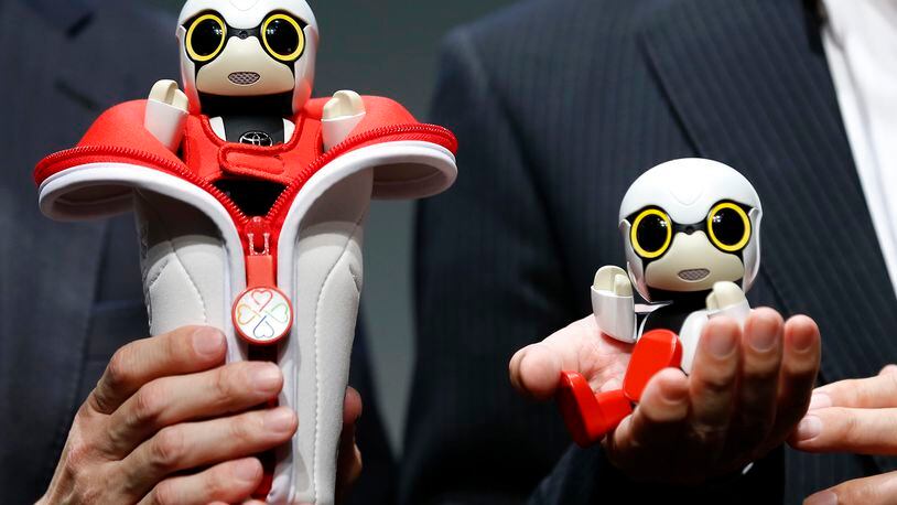 In this Sept. 27, 2016 photo, Toyota Motor Corp. SMO Moritaka Yoshida, right, and Fuminori Kataoka, project general manager from Toyota Motor Corp., pose for photographers with compact sized humanoid communication robots, Kirobo Mini, during a press unveiling in Tokyo. The new robot from Japanese automaker Toyota Motor Corp. can’t do much else but chatter in a high-pitched voice. (AP Photo/Shizuo Kambayashi)