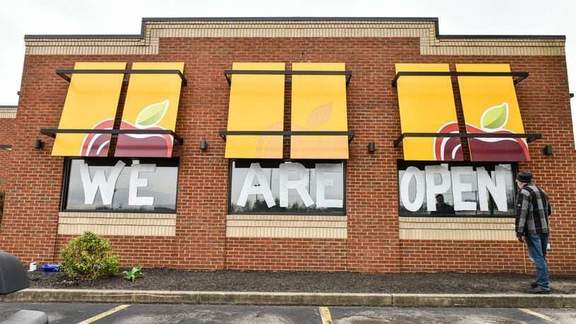 Jarett Trudel, general manager of Applebee’s in Hamilton, paints “We Are Open” on the side windows Tuesday, March 31 as a way to let people know they are still serving food. They are open 11 a.m. to 9 p.m. with for carryout orders by phone or web ordering. NICK GRAHAM / STAFF