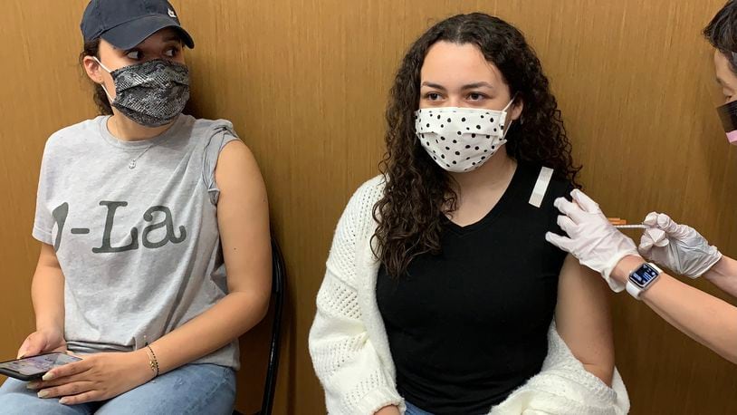 Camille Heard, 16, of Liberty Twp. gets her first dose of the coronavirus vaccine on Monday at the University of Dayton Arena while her 20-year-old sister Chloe Heard waits her turn.