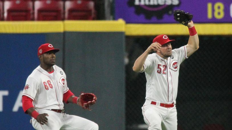 Reds second baseman Kyle Farmer, right, makes a catch in front of right fielder Yasiel Puig in the ninth inning against the Braves just after midnight on Friday, April 26, 2019, at Great American Ball Park in Cincinnati. David Jablonski/Staff