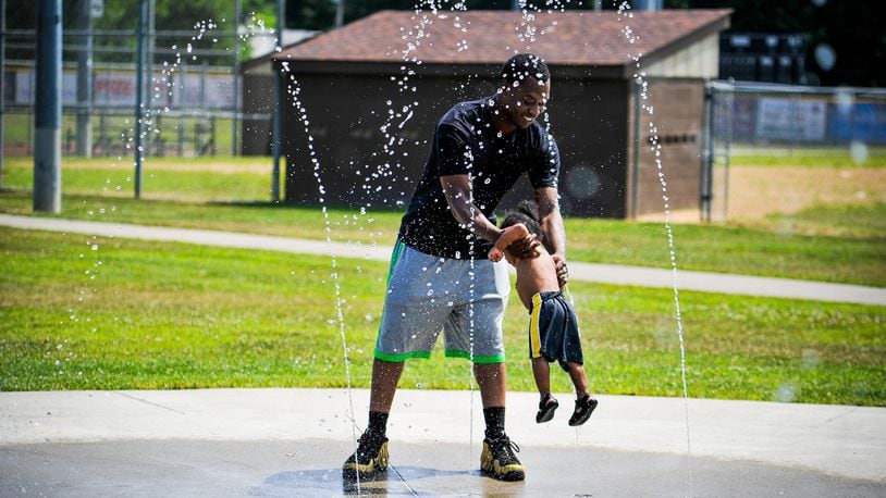 Brian Cleckley swings his son, Braxton Cleckley, 1, through the water at the splash pad outside the Booker T. Washington Community Center on S. Front Street Thursday, July 11 in Hamilton. Another heat wave is expected to hit Butler County this weekend with the heat index reaching above 100 degrees. NICK GRAHAM/STAFF