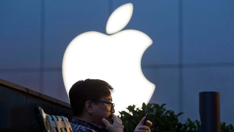 FILE - In this Friday, May 13, 2016, file photo, a man uses his mobile phone near an Apple store in Beijing, China. Apple Inc. reports financial results Tuesday, Jan. 31, 2017. (AP Photo/Ng Han Guan, File)