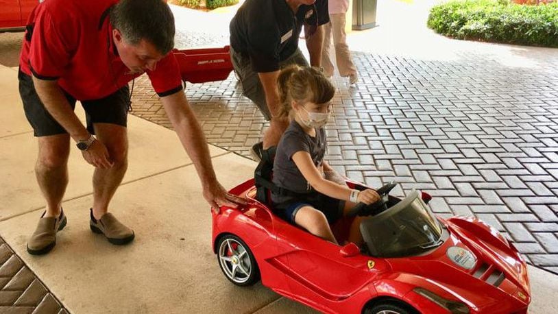 Brian Murphy, left, and Craig Kelley roll a mini-Ferrari convertible carrying 5-year-old Abigail Sporke into Palms West Hospital. Murphy and Kelley are with Little Smiles, which donated the car to the hospital's pediatric patients.
