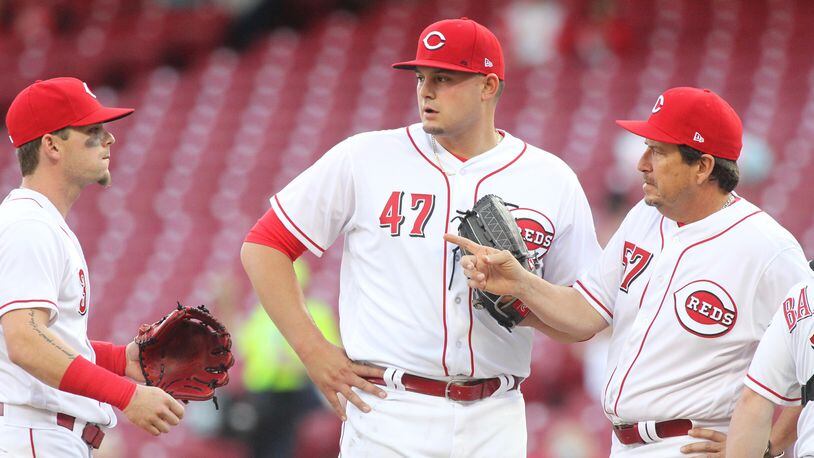 Reds starter Sal Romano, center, is visited by catcher Tucker Barnhart, far right, pitching coach Mack Jenkins, second from right, and Scooter Gennett during a game against the Cardinals on Thursday, April 12, 2018, at Great American Ball Park in Cincinnati. David Jablonski/Staff