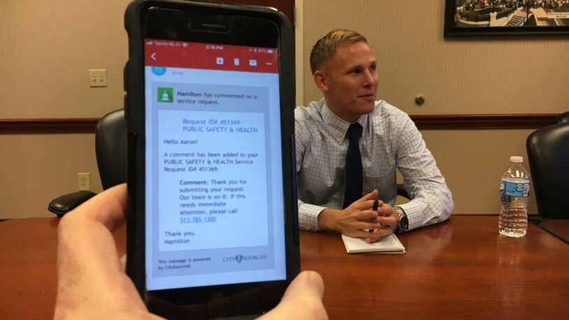 Hamilton city senior analyst Aaron Hufford describes the new 311 Hamilton App, while a phone shows a confirmation message that the app sends to someone who has sent a complaint, request for help, compliment or suggestion through the system, which goes online today. MIKE RUTLEDGE / STAFF
