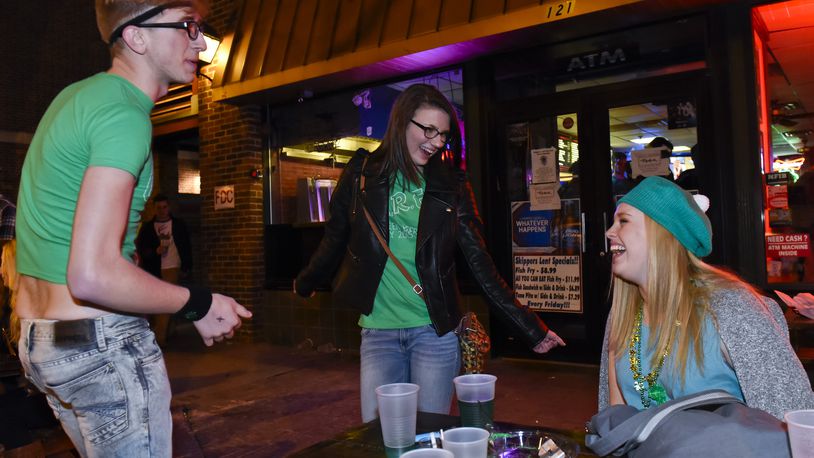 Jacob Rasmussen and Megan Kudej dance as Sidney Calicoat watches as they sit in front of Skippers before sunrise during Green Beer Day Thursday, March 19 in Oxford.  NICK GRAHAM/ STAFF