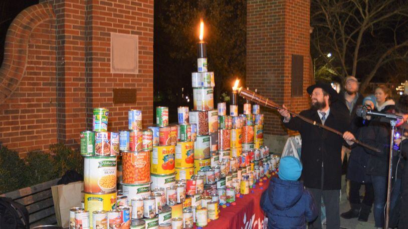 Rabbi Yossi Greenberg lights a candle on the Menorah created with cans of food which were later donated to the Oxford Community Choice Pantry. CONTRIBUTED/BOB RATTERMAN