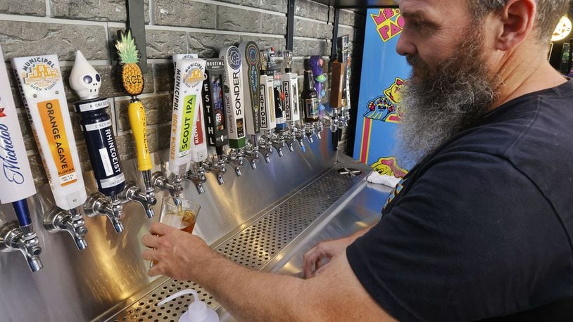 Pinball Garage owner Brad Baker pours a Municipal Brew Works beer, crafted by a fellow Hamilton business, Thursday, July 21, 2022, in Hamilton. Many businesses in Hamilton support each other in various ways. NICK GRAHAM/STAFF