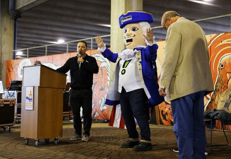Alexander, the 17 Strong mascot, stands between Jim Goodman with Municipal Brew Works, left, and Hamilton mayor Pat Moeller, right, during the state of the city address under the McDulin Parking Garage Thursday, May 5, 2022. The location was moved from the original location of Municipal Brew Works due to rain.  NICK GRAHAM/STAFF