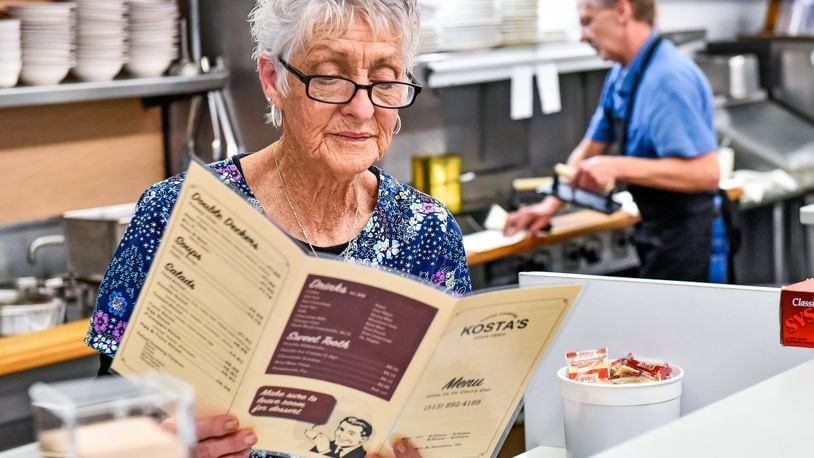 Wilma Gadd refreshes her memory of the menu while Wes Haggard prepares food on the grill at Kostas Restaurant on Tuesday, Nov. 5, 2019 in Hamilton. Gadd has worked at the restaurant for over 40 years and Haggard has worked there for 24 years. Kostas, under new ownership, reopened Tuesday after being closed for over a year. NICK GRAHAM/STAFF