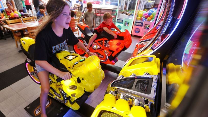 Jasmine Watkins, 11 and Dominic Watkins ride on a motorcycle game inside the new expansion at Pinball Garage in Hamilton. Pinball will be adding game machines to Spooky Nook Sports at Champion Mill in a new arcade there. FILE