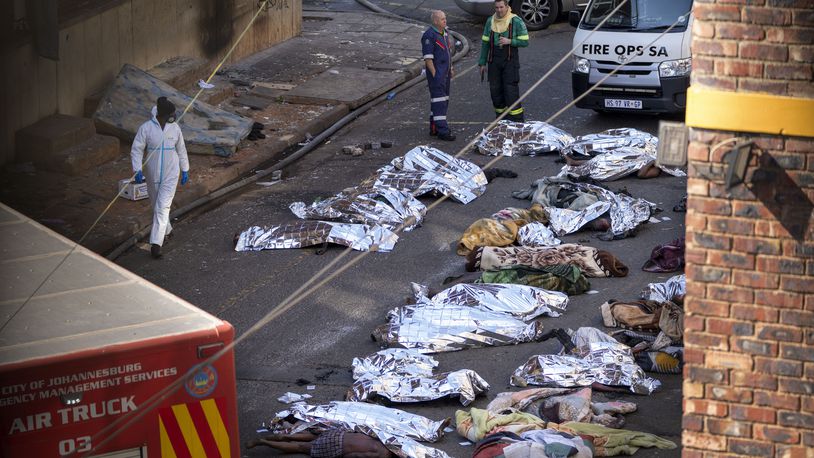 FILE - Medics stand by the covered bodies of victims of a deadly blaze in Johannesburg, Thursday, Aug. 31, 2023. A report into a building fire that killed 76 people in South Africa last year has concluded that city authorities should be held responsible because they were aware of serious safety issues at the rundown apartment block at least four years before the blaze. The nighttime fire at the five-story building in downtown Johannesburg on Aug. 31 was one of South Africa's worst disasters. At least 12 children were among the dead and another 86 people were injured. (AP Photo/Jerome Delay/File)