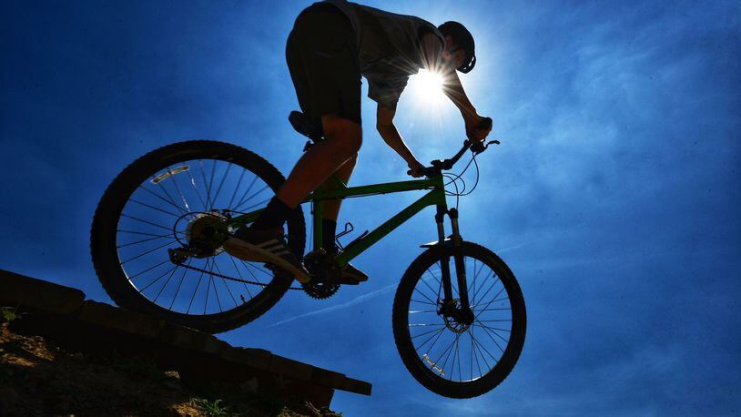Reece Jackson, from Morrow, rides his bike on the jump line silhouetted in the sun at Premier Health Atrium Medical Center Bike Park Monday, July 1 in Lebanon. NICK GRAHAM/STAFF