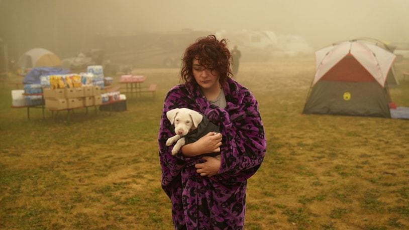 Shayanne Summers holds her dog Toph while wrapped in a blanket after several days of staying in a tent at an evacuation center at the Milwaukie-Portland Elks Lodge, Sunday, Sept. 13, 2020, in Oak Grove, Ore. "It's nice enough here you could almost think of this as camping and forget everything else, almost," said Summers about staying at the center after evacuating from near Molalla, Oregon which was threatened by the Riverside Fire. (AP Photo/John Locher)