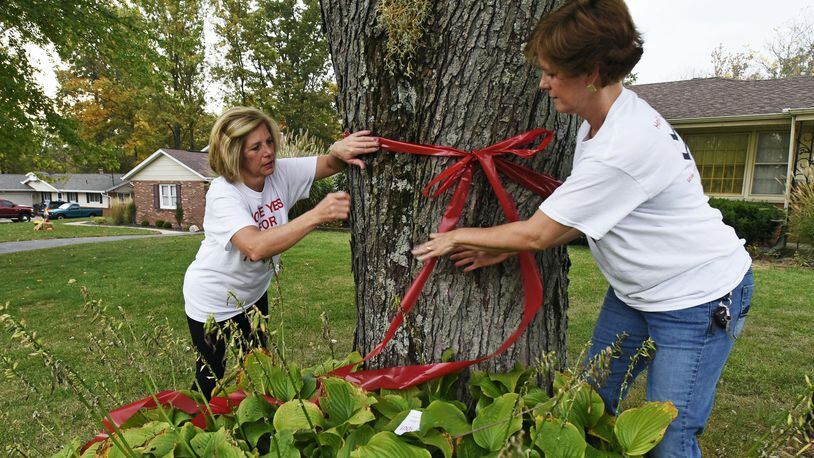 Diana Ramsey, left, and Kelly Derickson tie a red ribbon around a tree on Wednesday at a home in Hanover Twp. after speaking with the homeowner about the upcoming levy vote. The two were going door-to-door asking residents who support its fire levy request, and its operation levy, to tie a red ribbon around a front-yard tree to show support.