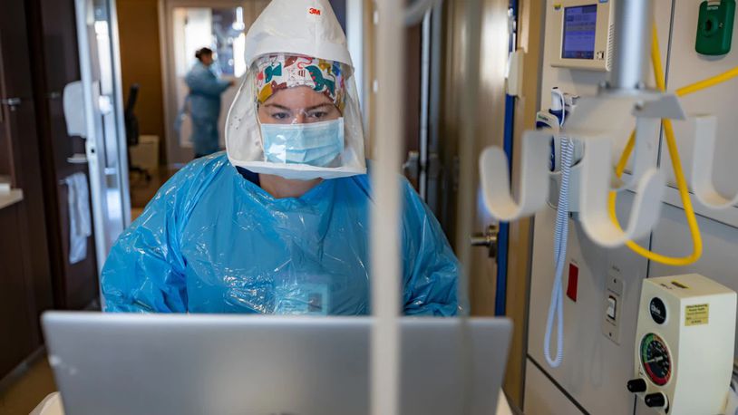 Taylor Spicer is a nurse at Miami Valley Hospital nurse. She is wearing full personal protective equipment, including an oxygen tank on her back, as she enters data for a COVID-19 patient in the hospital's COVID-19 unit.