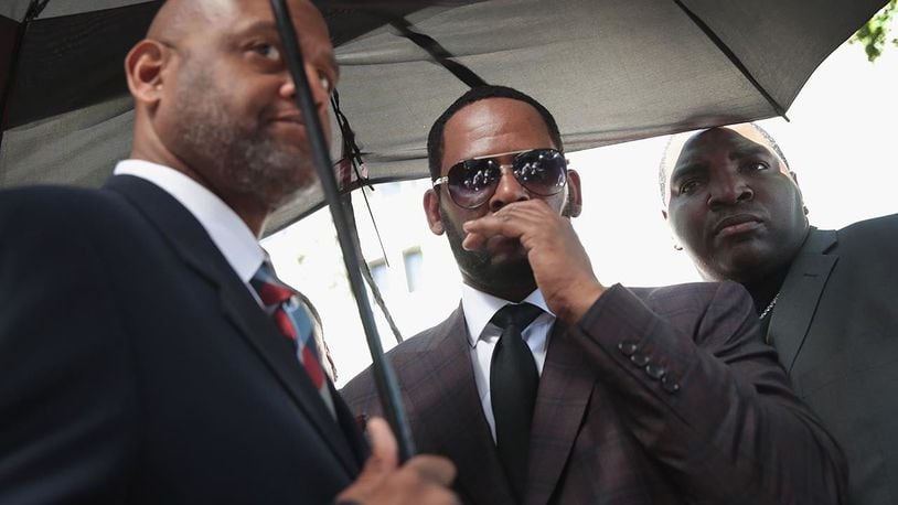 Singer R. Kelly covers his mouth as he speaks to members of his entourage as he leaves the Leighton Criminal Courts Building following a hearing on June 26, 2019 in Chicago.