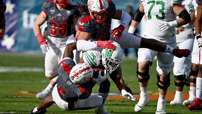 Miami defensive back Cecil Singleton (2) and defensive lineman Kameron Butler (82) tackle North Texas running back Ikaika Ragsdale (25) in the first half of the Frisco Football Classic NCAA college football game in Frisco, Texas, Thursday, Dec. 23, 2021. (AP Photo/Matt Strasen)