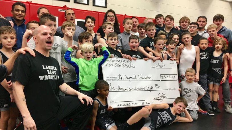 Lakota East High School Youth Wrestling Coach Jay Zurlinden, left, presented a $3,700 check to Dragonfly Foundation co-founder Ria Davidson, back row center, Tuesday evening. Zurlinden’s 10-year-old son Jayden, third from right first row standing, is a cancer survivor and now wrestler. MICHAEL D. CLARK