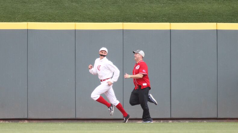 The Stache, left, races a fan during a game between the Reds and the Brewers on Tuesday, April 2, 2019, at Great American Ball Park in Cincinnati.