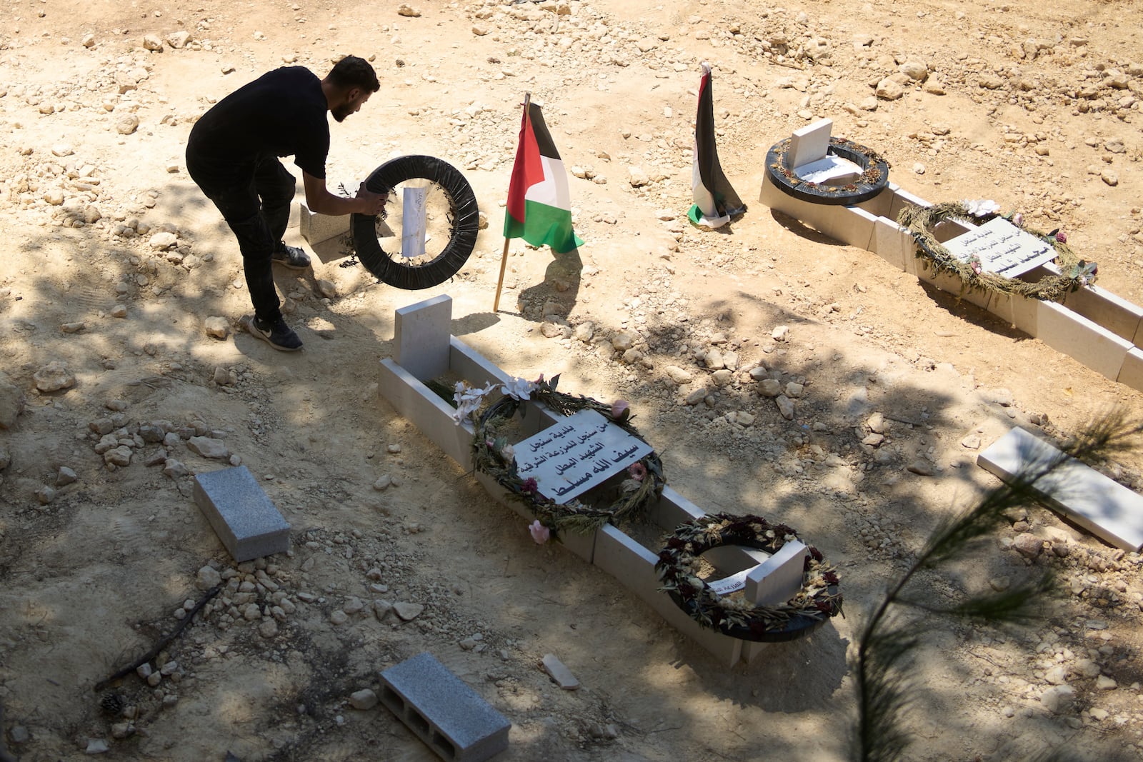 On Monday, July 21, 2025, a man tidies the graves of Palestinian-American Sayfollah Musallet, left, and Mohammed al-Shalabi, both of whom were killed by Israeli settlers in the West Bank town of Al Mazra as-Sharqiya. (AP Photo/Maya Alleruzzo)